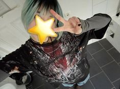 a person with green hair holding a star shaped object in front of their face and making the peace sign