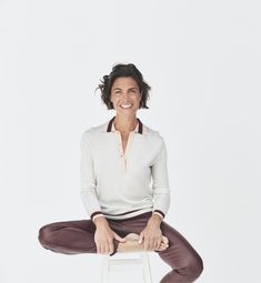 a woman sitting on top of a white stool with her legs crossed and smiling at the camera