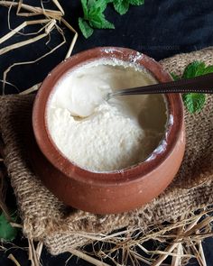 a bowl filled with cream sitting on top of a table next to straw and green leaves