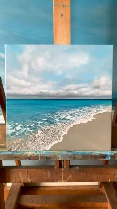 an easel with a painting on it in front of the ocean