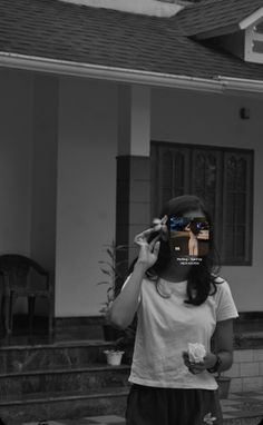 a woman standing in front of a house holding a camera up to her face