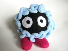 a black and blue stuffed animal with two eyes on it's head, sitting on a white surface