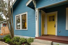 a blue house with yellow door and steps leading up to the front door, next to a tree