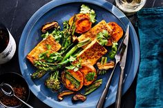 a blue plate topped with tofu and veggies next to two glasses of wine