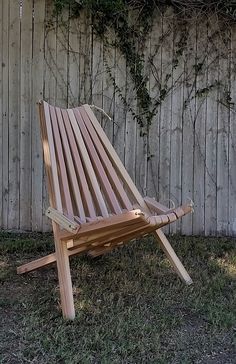 a wooden chair sitting in the grass near a fence