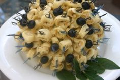 a white plate topped with pasta covered in olives and black olives next to a green leaf