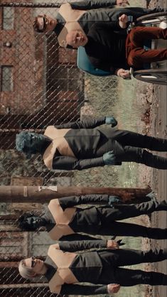 three men in suits and ties standing next to each other near a chain link fence