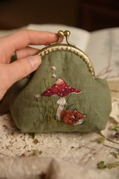 a hand is holding a small green purse with a red mushroom on the front and a fox on the back