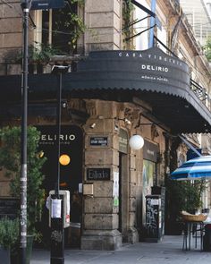 an outdoor cafe with tables and umbrellas on the side of the street in front of it