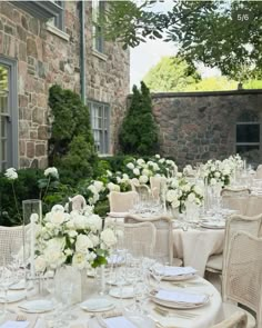 a table set up with white flowers and place settings for an outdoor wedding reception in front of a stone building