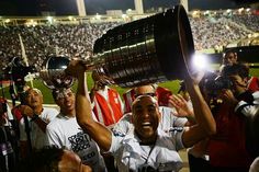 a group of people holding up trophies in front of a crowd at a baseball game