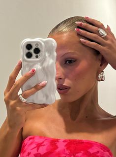 a woman in a pink dress holding her phone up to her face with both hands