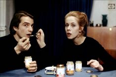 a man and woman sitting at a table with jars in front of them eating food