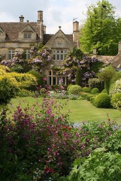 a large house surrounded by lush green grass and flowers in front of it, with trees and bushes surrounding the building