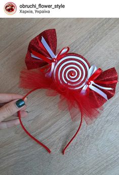 a hand holding a red and white candy cane headband on top of a wooden table