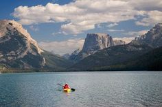 a person in a kayak on the water with mountains in the background