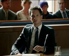 a man in a suit and tie sitting at a table with other people behind him