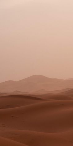 two people riding horses through the desert on a foggy day with mountains in the background