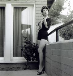 a woman leaning on the side of a building while talking on a cell phone and wearing high heels