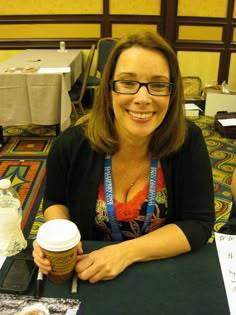 a woman sitting at a table with a cup of coffee in front of her smiling