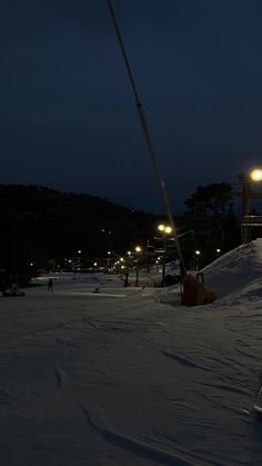 a man riding skis down a snow covered slope at night with street lights on