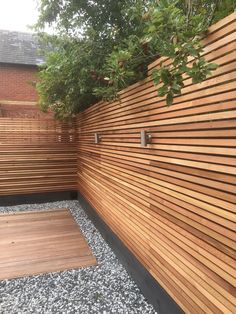 a wooden fence next to a tree and gravel area with rocks on the ground in front of it