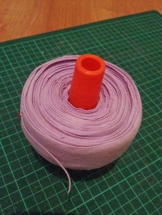 a spool of purple thread sitting on top of a green cutting mat next to an orange piece of cloth