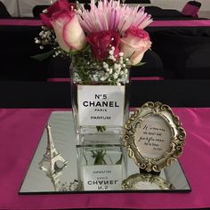 pink flowers in a vase on top of a table with perfume bottles and other items