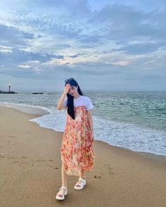 a woman standing on top of a sandy beach next to the ocean with her head in her hands