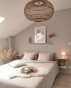 a white bed sitting under a light fixture in a bedroom next to a lamp shade