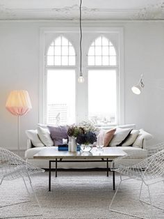 a living room filled with white furniture and two large windows in the wall behind them