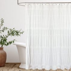 there is a white shower curtain next to a bathtub and a potted plant