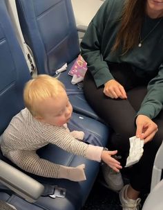 a woman sitting on an airplane with a toddler in it's lap playing with money