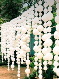 a bunch of white balls hanging from the side of a building in front of trees