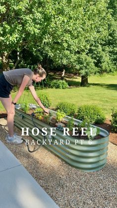 a woman is bending over to plant some plants in her raised garden bed with the words hose reel backyard plot