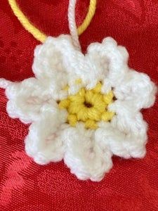 a crocheted flower ornament hanging on a red fabric material with yellow and white thread