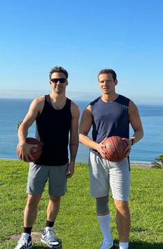 two men standing next to each other on top of a lush green field holding basketballs