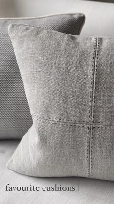 two gray pillows sitting on top of a white couch