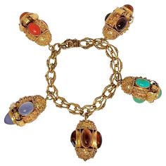 This fanciful vintage creation is uniquely the product of master goldsmiths working in Italy during the Mid-20th Century. Mounted on the very intricate bracelet of the same period are five very detailed and handmade Etruscan Revival charms, each set with numerous precious stones. Included are Mediterranean orange coral, dyed chalcedony, turquoise and Baltic Amber. Average charm length is 1 3/8 inches and bracelet length is 7 1/2 inches. The bracelet and the bale to each individual charm are stamped 750, designating 18k gold. Gross weight 114 grams. Etruscan Jewelry, Solid Gold Charms, Locket Bracelet, Orange Coral, Gold Charm Bracelet, Locket Charms, Bangle Bracelets With Charms, Body Jewellery, Baltic Amber