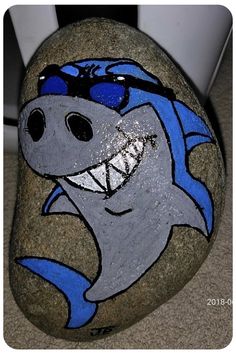 a painted rock with a shark wearing sunglasses on it's face and smiling for the camera