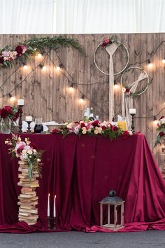 the table is covered with red cloth and decorated with flowers, greenery and candles