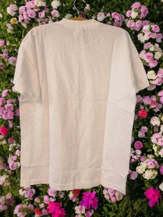 a white t - shirt hanging in front of flowers