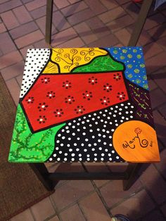 a child's wooden chair painted with different colors and designs on it, sitting on the ground