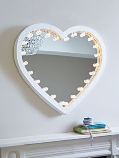 a heart shaped mirror on the wall next to a fire place with books and a candle