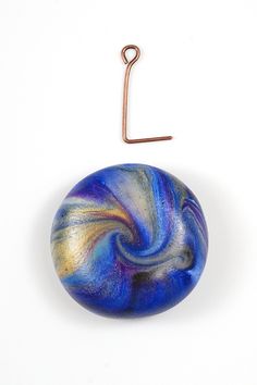 a blue and gold swirl bead hanging from a hook on a white surface with a metal hook