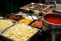 many different types of pasta in trays on a buffet table with sauce and condiments