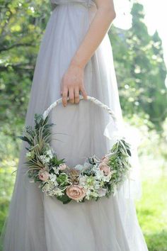 a woman in a white dress holding a basket with flowers and greenery on it