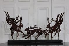 three metal deer sculptures sitting on top of a black table next to a white door