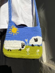 a crocheted purse with sheep on it hanging from a hook in front of a white t - shirt