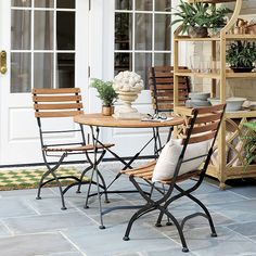 an outdoor table and chairs with potted plants on the outside wall behind them, in front of a white door